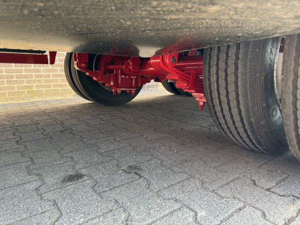 Schilderwagen met rode hydraulische onderdelen en grote banden onder de vrachtwagen.
