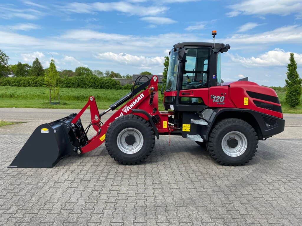 Rode Yanmar stage V wheeled loader op betonnen bestrating met groene achtergrond en blauwe hemel.