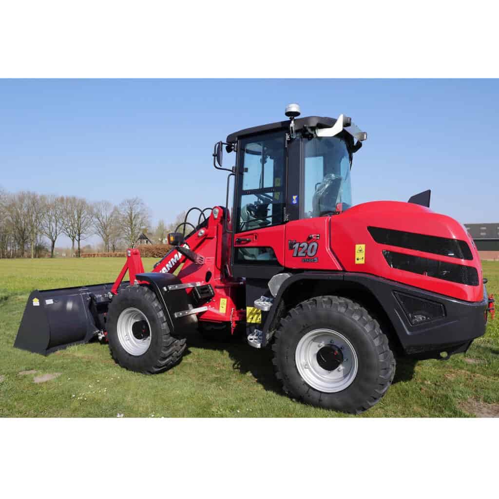 Zware rode wiellader op veld met blauwe lucht en bomen op achtergrond.