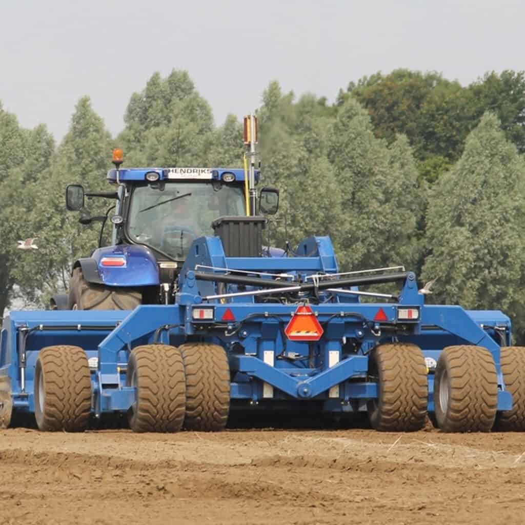 Extreem brede schoffel financieel zwaar landbouwvoertuig in actie op een akker.