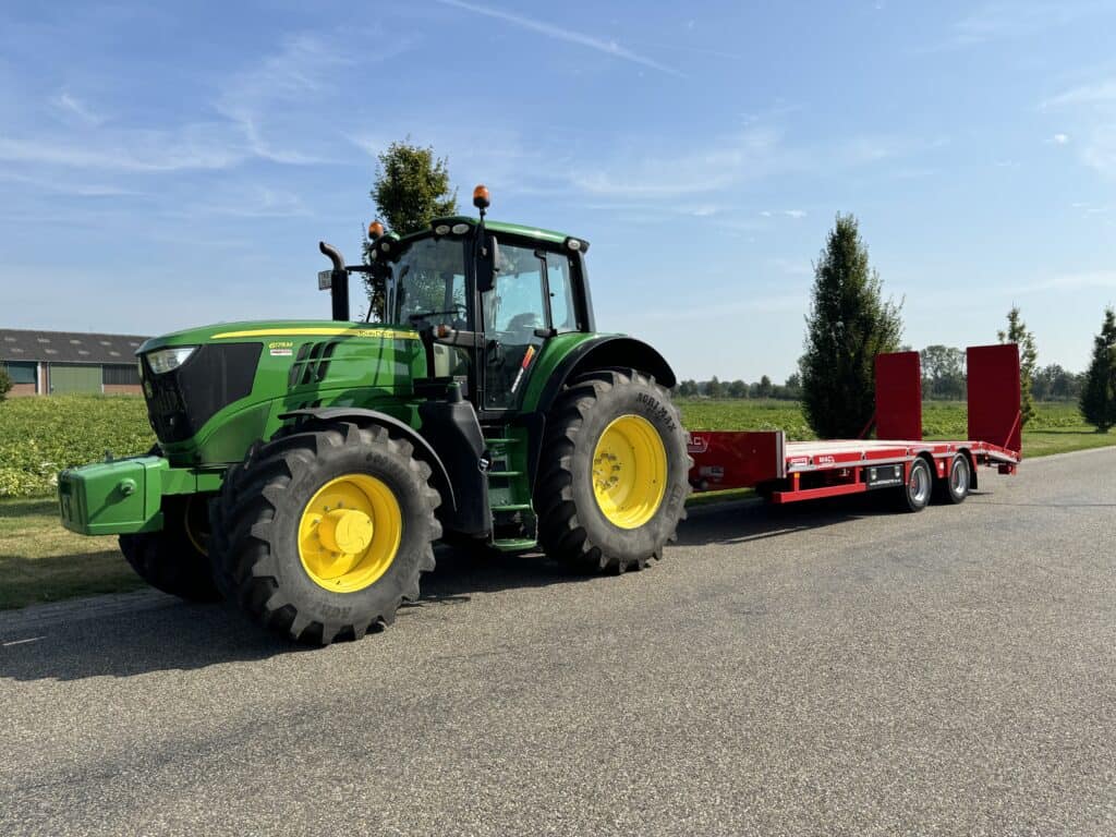 Luchtfoto van een groene John Deere tractor met een rood transportvoertuig op een landelijke weg in Nederland.