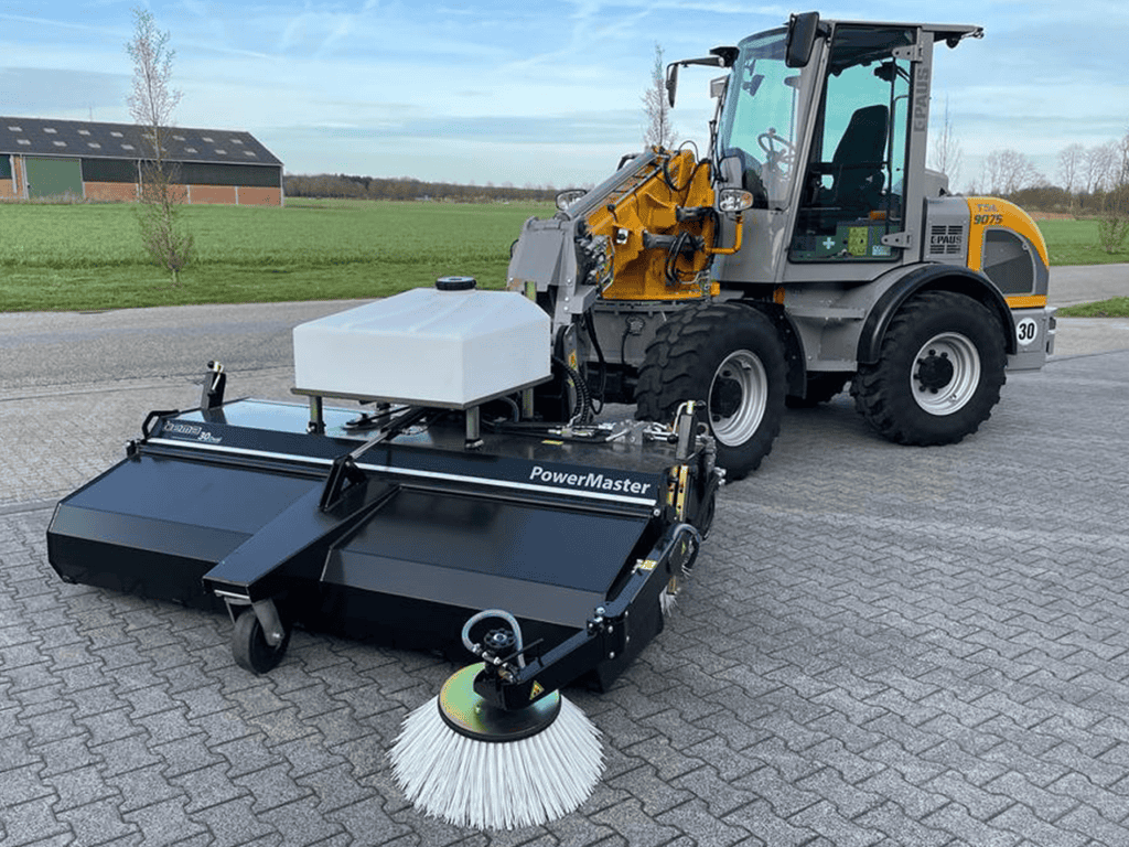 Veegmachine voor straatreiniging aangesloten op een compacte wiellader, ideaal voor schoonmaakwerkzaamheden.