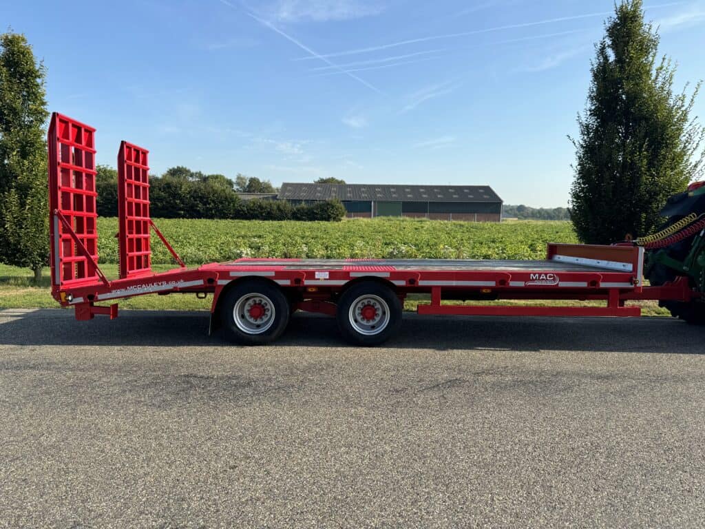 Veetransportwagen voor landbouwmachines op asfaltweg, rood, gestapelde laadkleppen.