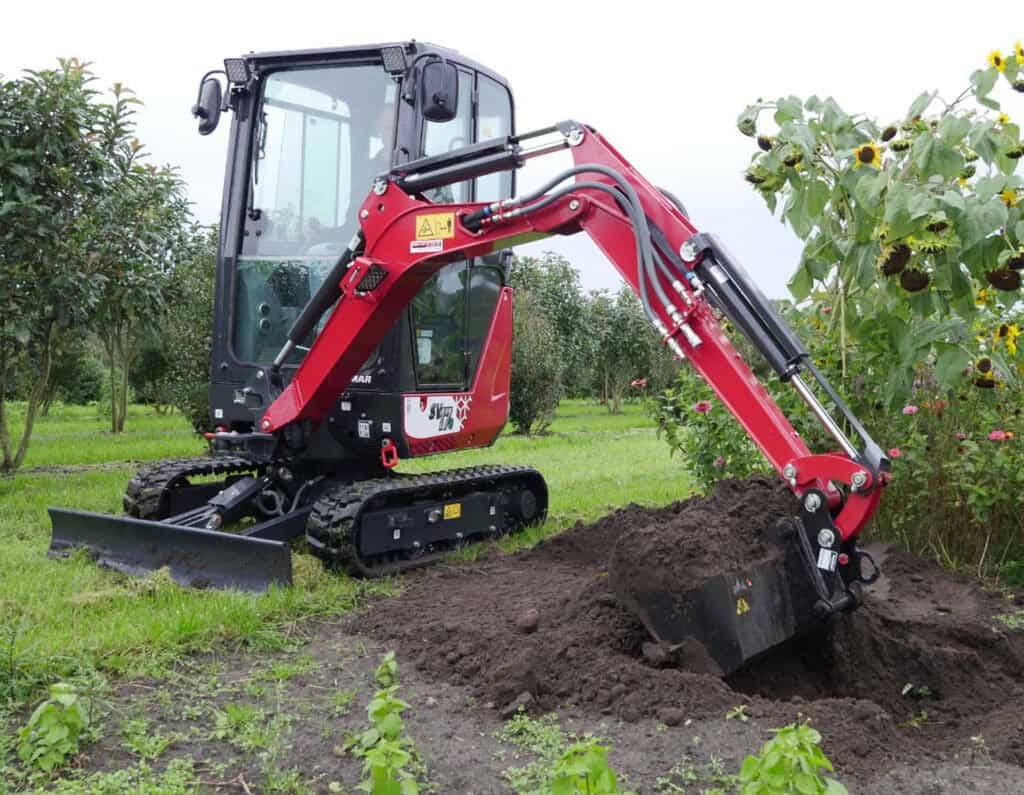 Kleine rode graafmachine op een grasveld, geschikt voor tuin- en landbouwwerkzaamheden.