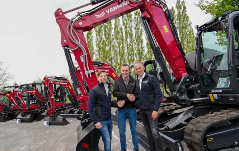 Three men in jackets shake hands in front of red Yanmar excavators at a dealership lot, posing for a photo.