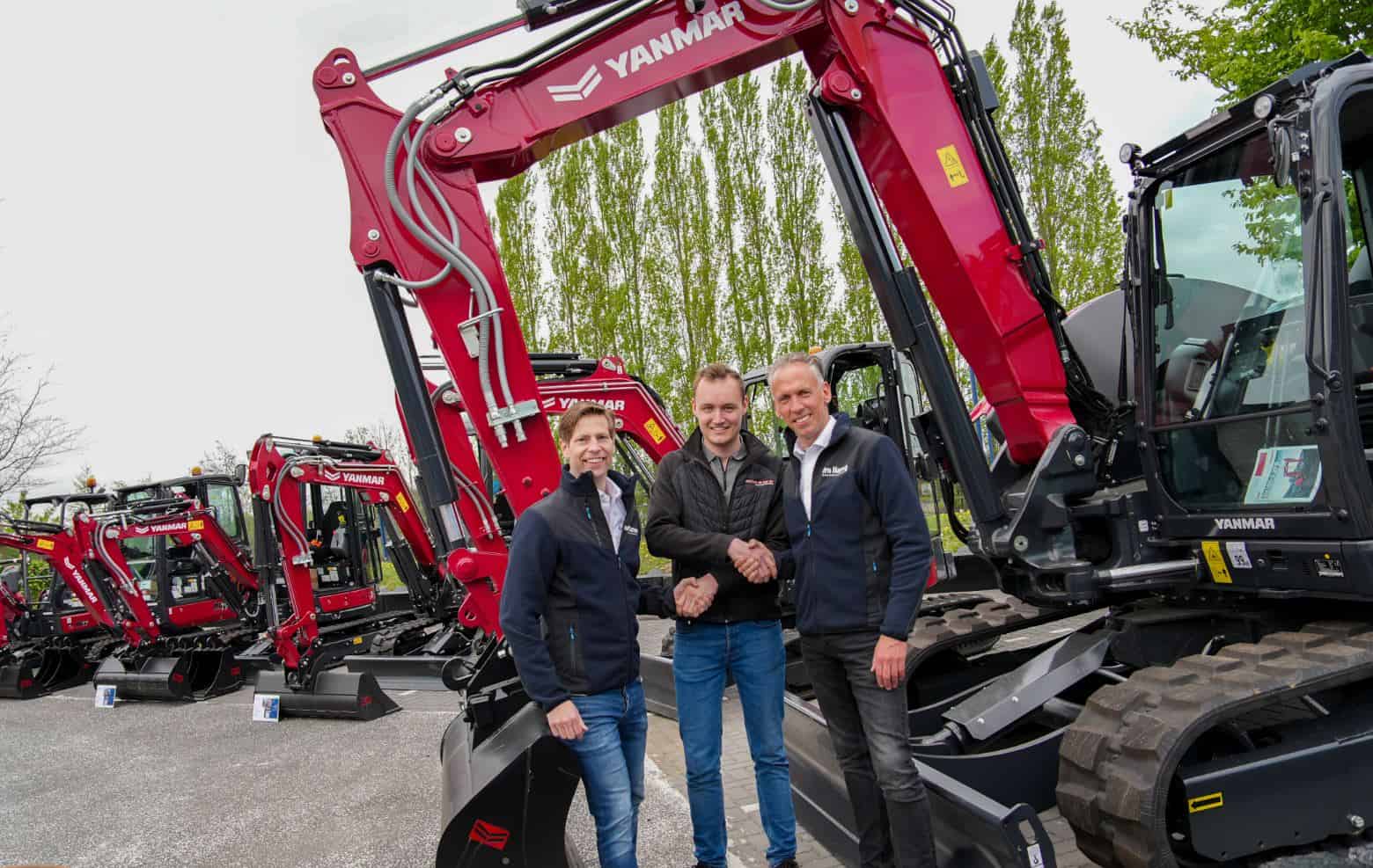 Three men in jackets shake hands in front of red Yanmar excavators at a dealership lot, posing for a photo.