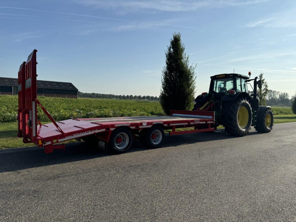 Zware landbouwtrailer getrokken door tractor op landelijke weg met agrarisch landschap.