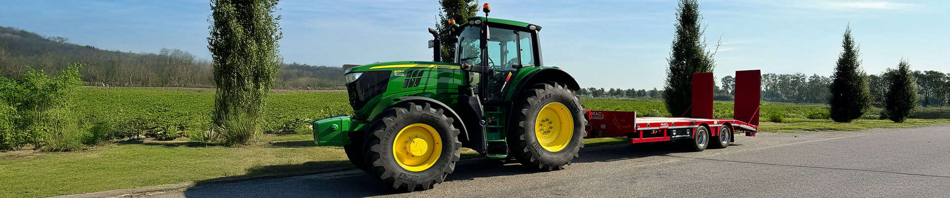 Groen tractor met rode transporteertand op landweg in groen landschap.