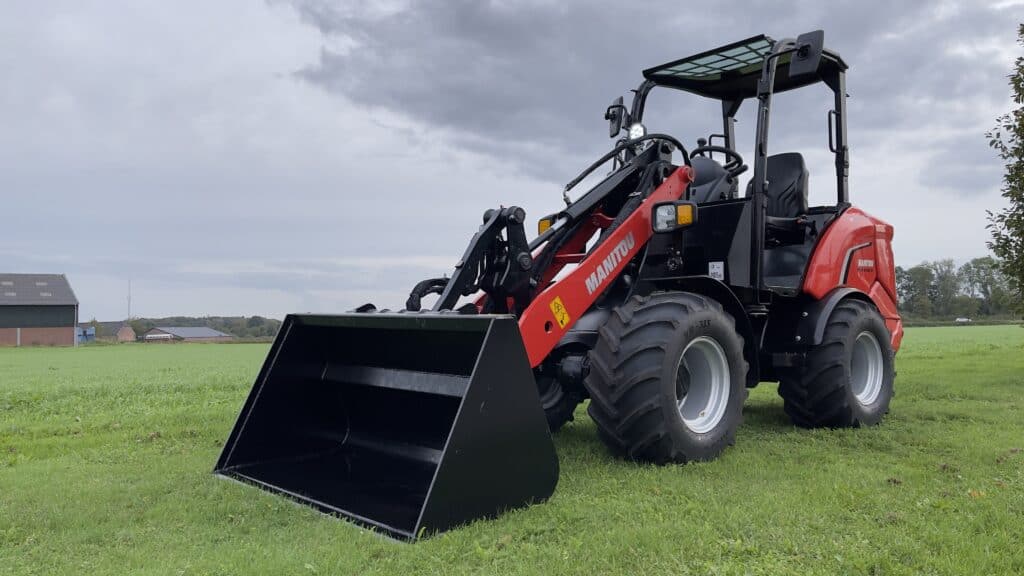 Klein landbouwtelessenedrieëbladige tractor met laadbak op grasveld.