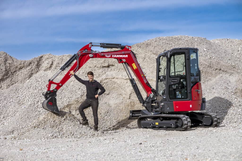 Kleiner hijskraan op bouwterrein met man in zwart jas en bouwhelmen.