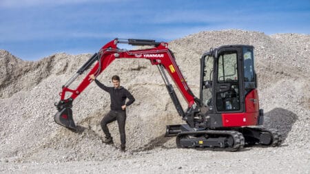 Kleiner hijskraan op bouwterrein met man in zwart jas en bouwhelmen.