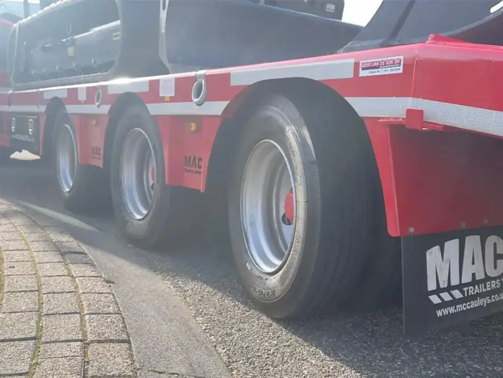 Stalen vrachtwagenoplegger met rode kleuren en meerdere wielen, geschikt voor transport en laden.