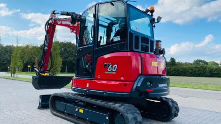 Kleine geavanceerde minigraver op oprit met groene omgeving en blauwe lucht.