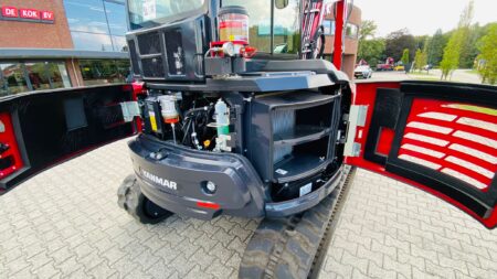 Compacte minigraafmachine met open motorkap, geschikt voor tuin- en bouwprojecten.