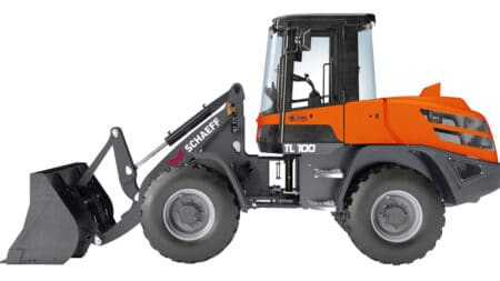 Front-end loader (Schaeff TL 100) with an orange cab and black bucket attachment ready to scoop material outside the frame far left-side view