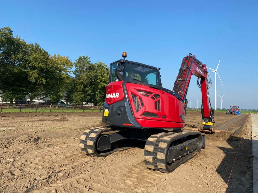 Klein graafmachine op een bouwplaats met windmolens op de achtergrond.
