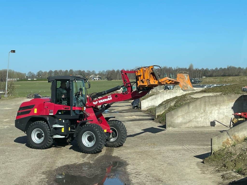 Verhoogde foto van een telescoop loader van Yanmar in bedrijf op een bouwplaats met betonwanden.