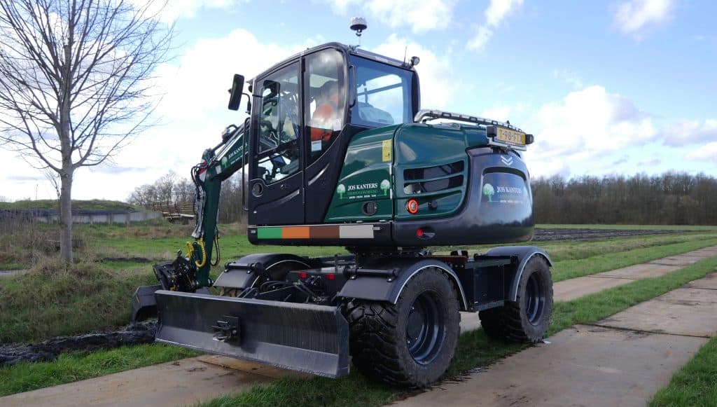 Mobiele graafmachine met logo van JOS KANTERS Groene Tuin en Groenvoorziening op ringbaan.