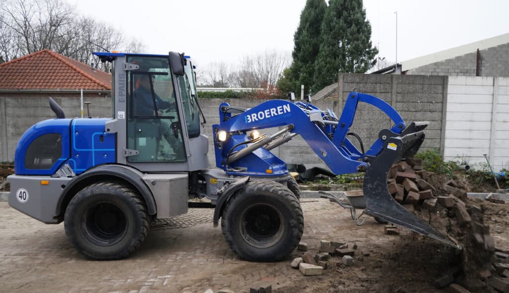 Zwaar bouwmaterieel: graafmachine voor wegen- en bermwerken, met logo 'Broeren Civil Solutions'.