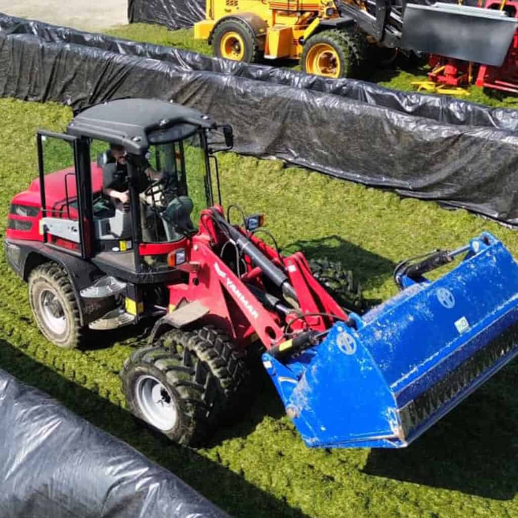Kleine landbouwtractor met blauwe frontlader op groene grasgrond.