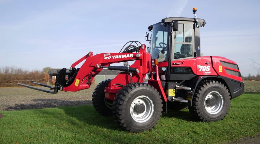 Kompakte rode Yanmar frontlader tractor op een grasveld.